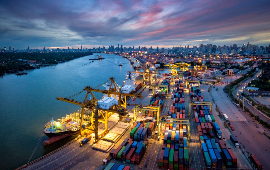 Aerial view of international port with Crane loading containers in import export business logistics with cityscape of Bangkok city Thailand at night